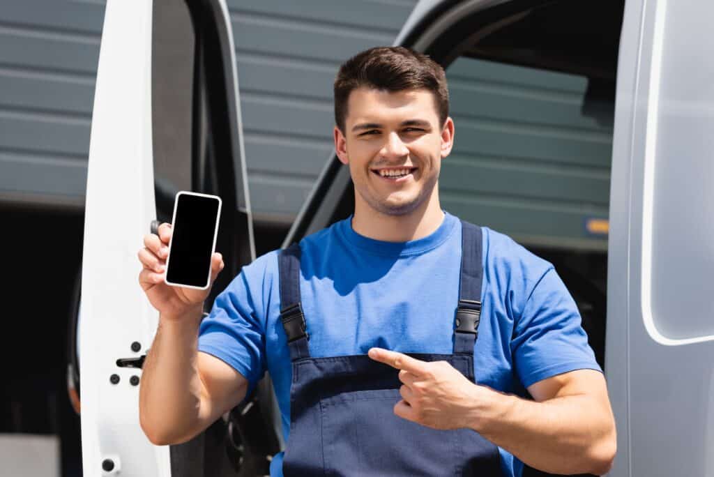 Loader pointing with finger at smartphone with blank screen near truck outdoors