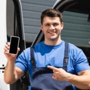 Loader pointing with finger at smartphone with blank screen near truck outdoors